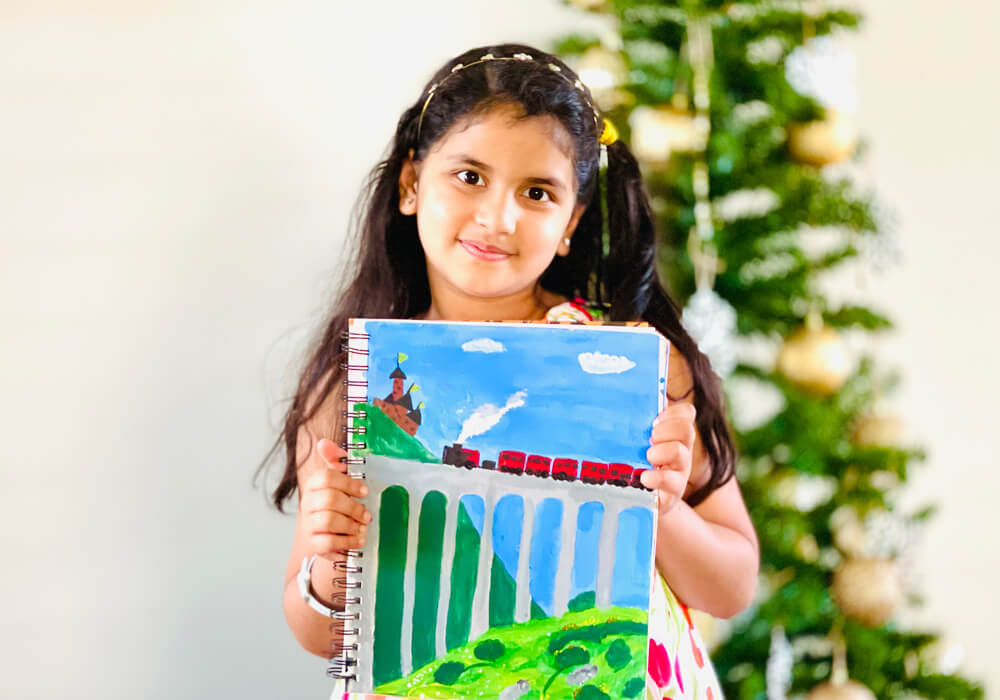 Ardra Ragesh with her Hogwarts express completed at Nimmys Art online art classes with a Christmas tree in the background