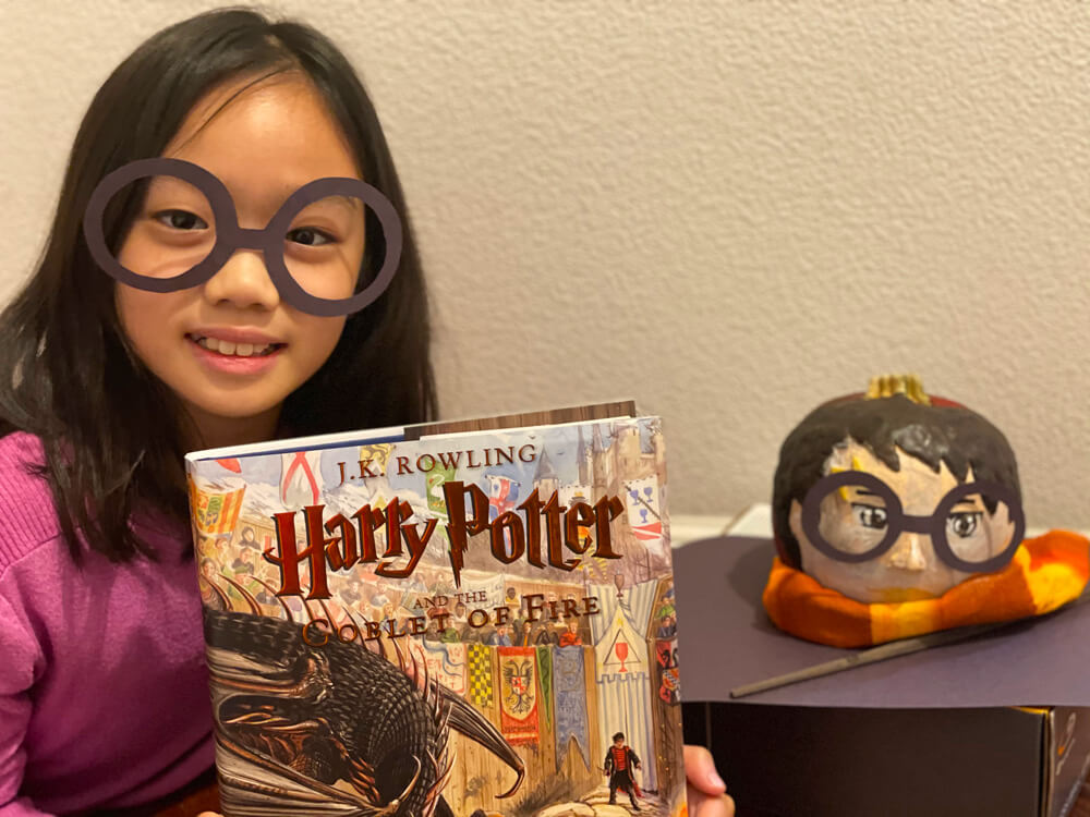 Abigail with her Harry Potter and the Goblet of Fire book, and the Halloween craft that won her the prize at the Halloween Pumpkin Art Contest in her neighborhood.