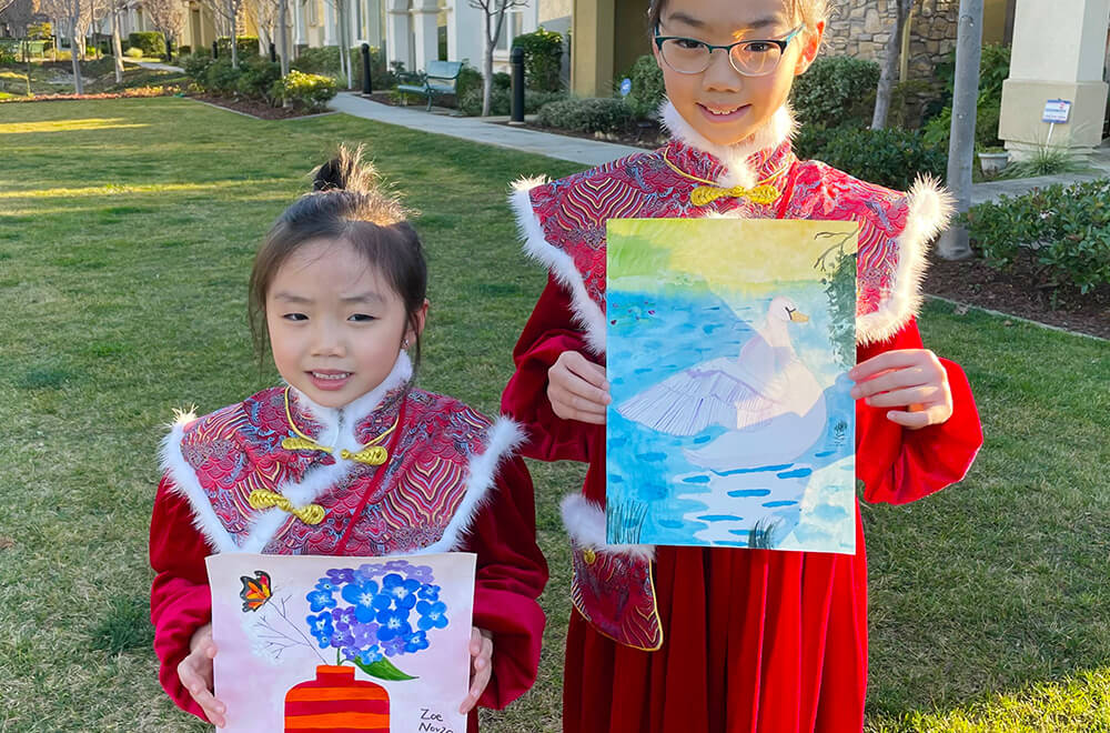 Zoe and her sister Abigail dressed in traditional attire with their artworks from Nimmy's Art