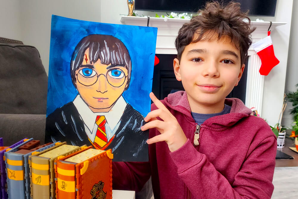 Image of a boy proudly displaying his Harry Potter painting from Nimmy's Art class. 
