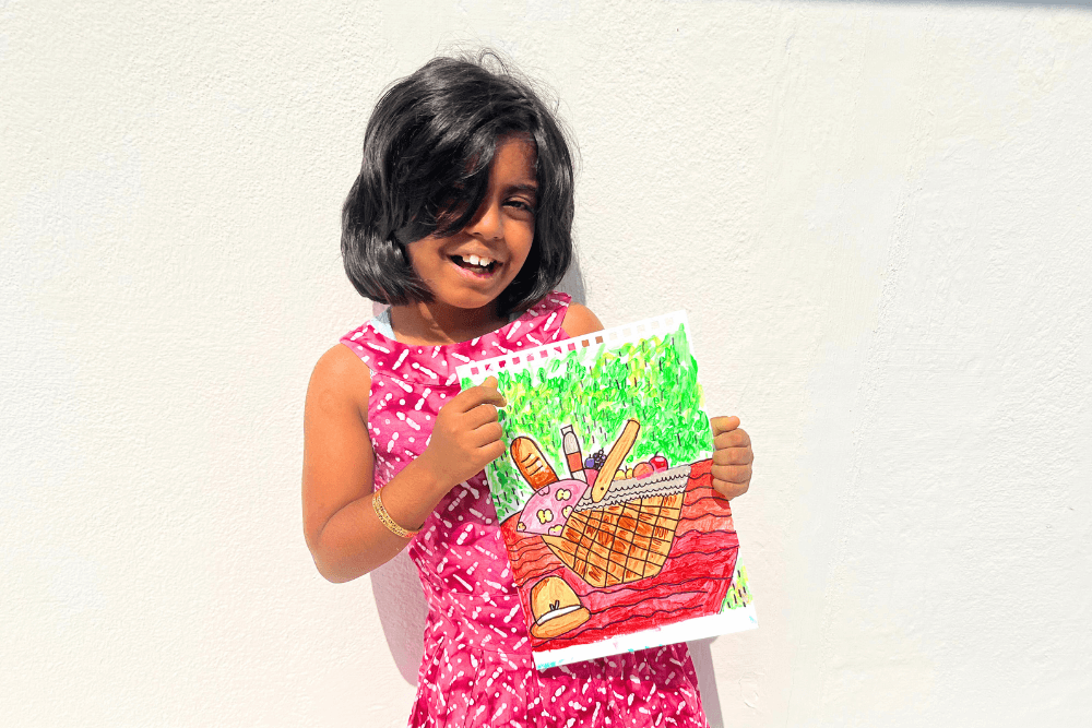 This image features a talented young artist proudly holding her vibrant Acrylic painting – a captivating Still Life of a Picnic Basket. Immerse yourself in the world of creativity and skill nurtured by Nimmy's expert guidance.