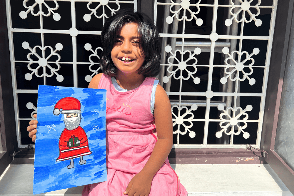 A young artist joyfully holding her acrylic painting, 'A Gift From Santa.' Immerse yourself in the world of creativity and expression with Nimmy's expert guidance.