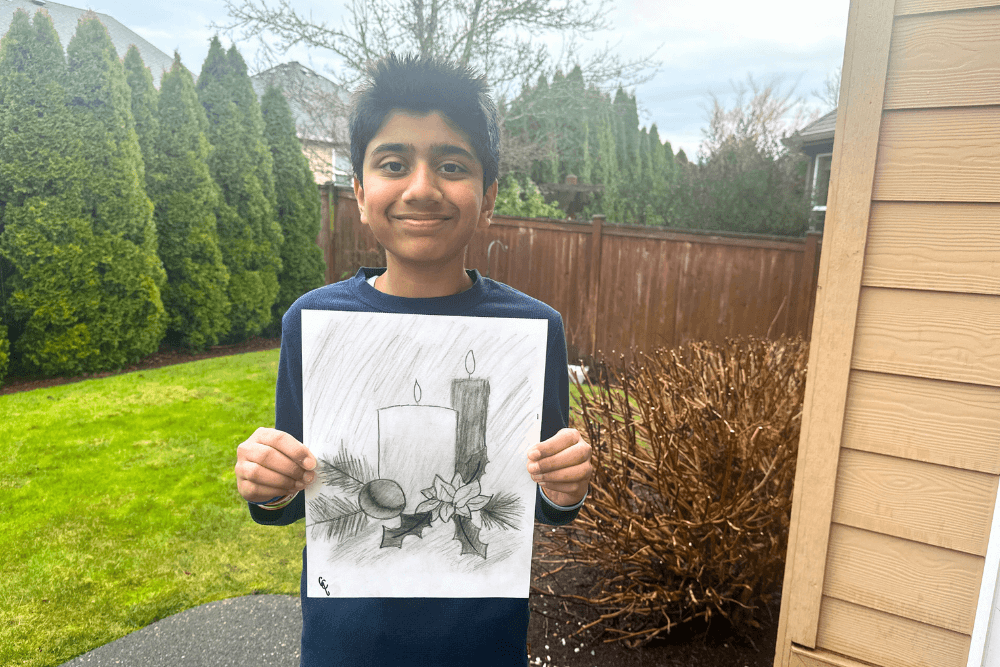 Young artist proudly holding charcoal drawing of holiday candles.