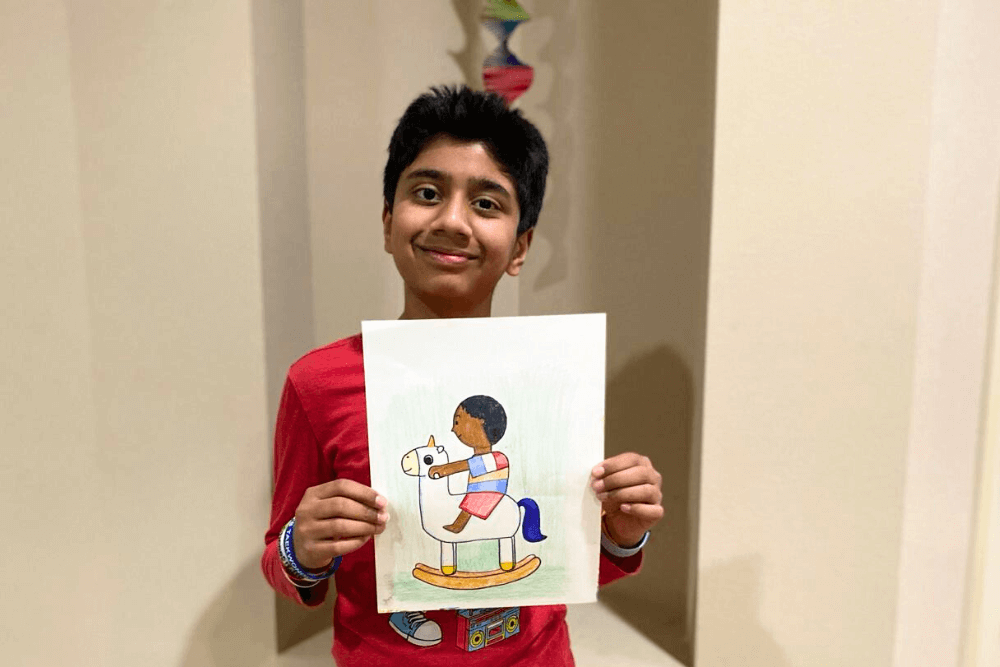 A young artist proudly holds his vibrant unicorn rocking chair drawing, showcasing artistic talent with Prismacolors in a step-by-step tutorial.