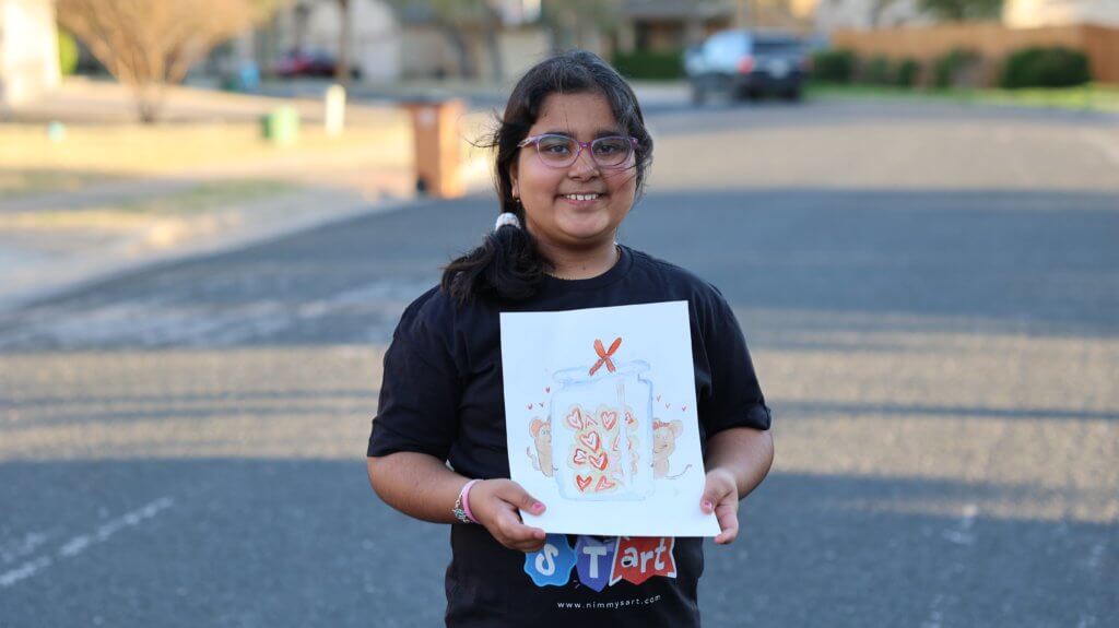 An artist holding up her painting of a jar filled with heart-shaped Valentine's Day cookies.