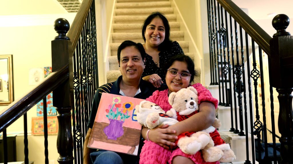 Navya, an artist, sits on the stairs with her parents beside her, sharing a moment of support and encouragement.