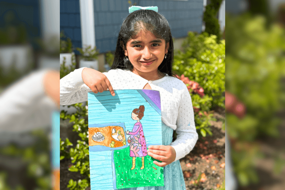 Dhanvi proudly holding her Thanksgiving-themed acrylic painting with a big smile.