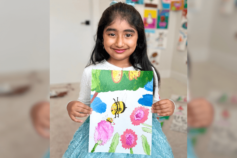 Dhanvi proudly holding her World Bee Day artwork painted with acrylics, featuring a vibrant bee and flowers.