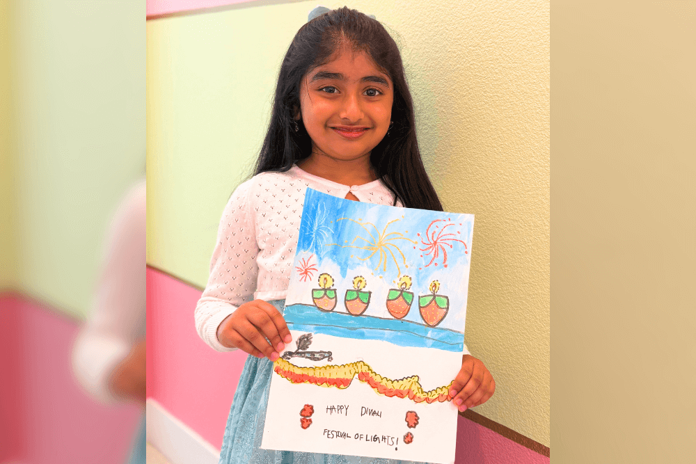 Dhanvi proudly holding her Festival of Lights artwork made with oil pastels, glowing with vibrant colors.