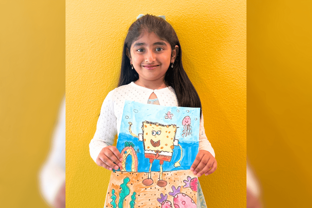 Dhanvi proudly holding her SpongeBob watercolor artwork created during Nimmy’s Art Summer Camp.