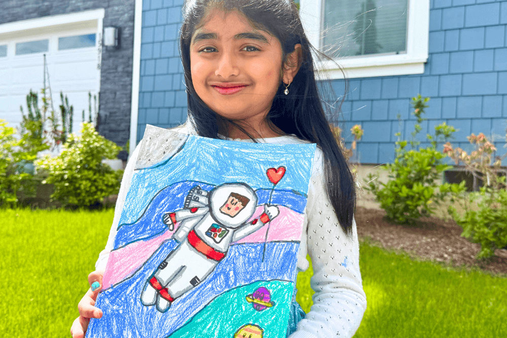 Dhanvi proudly holding her Galaxy Voyager artwork made with oil pastels, filled with vibrant space colors.
