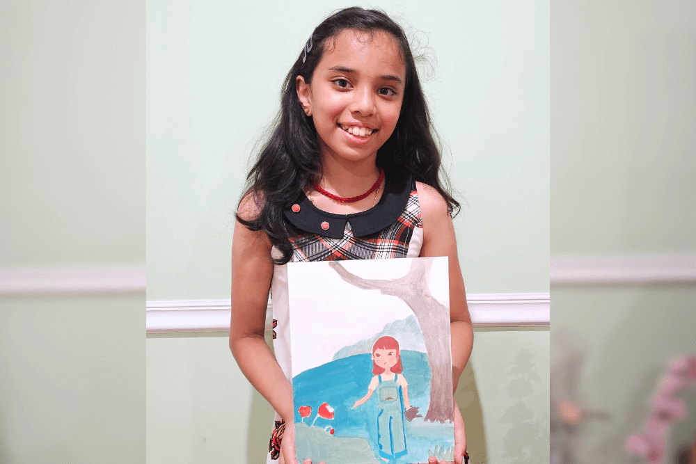 Young artist Uma smiling while holding a gouache painting of a girl in a blue dress standing near a tree, surrounded by bees and nature, suggesting a “Save the Bees” theme.  