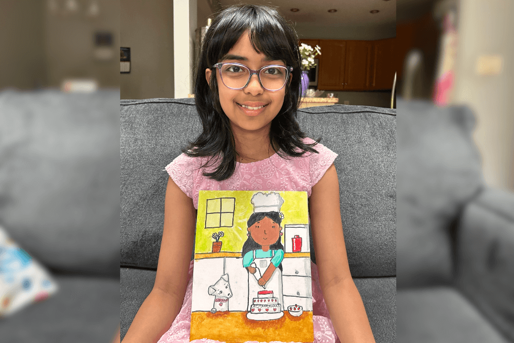 Aadhya holding her acrylic painting Baking Time with a girl chef and a dog in a playful kitchen scene.