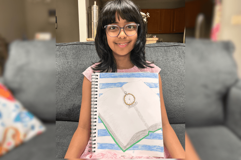 Aadhya holding her Prismacolor pencil drawing of a pocket watch on an open book, created during Summer Art Camp 2025.