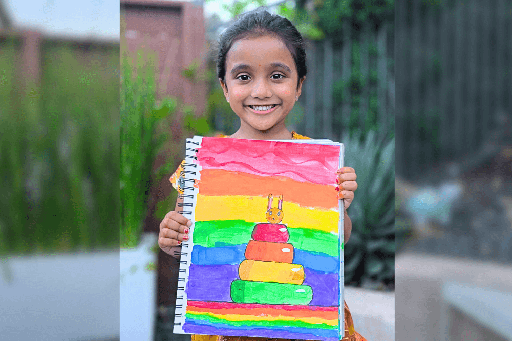 Aanya holding her acrylic painting Rainbow Stacking Toy with bright rainbow colors.