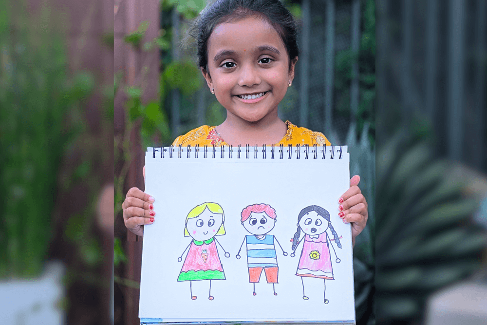 Aanya holding her pencil drawing Doodle Faces showing three children with different expressions.