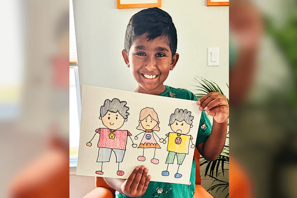 Young artist Avyaan holding his doodle faces drawing made with color pencils, showing basic expressions.