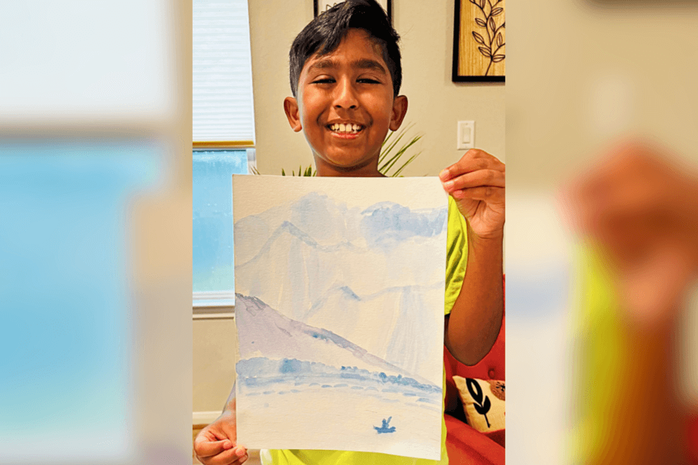Avyaan holding his watercolor painting of a lakeside landscape, showing gradients in color.