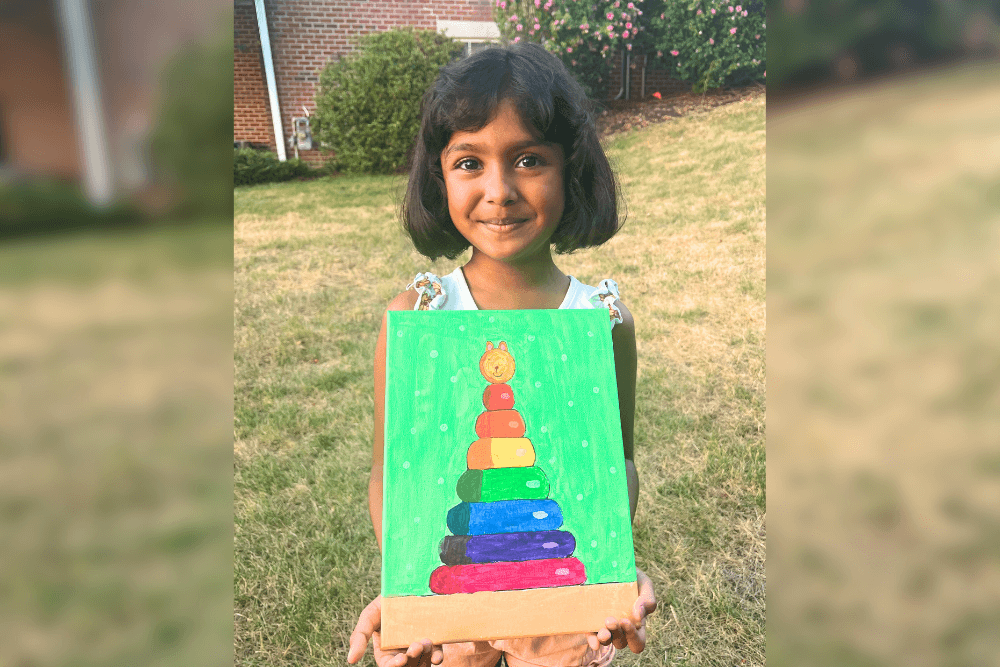 Charvi holding her colorful acrylic painting of a rainbow stacking toy with a pink and gold background. From summer art camp.