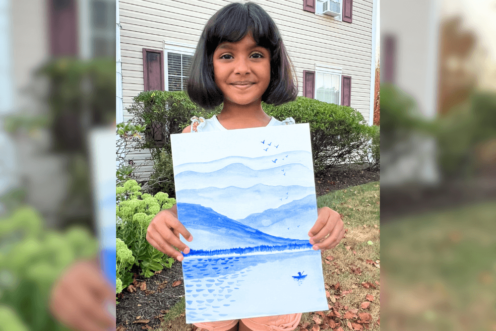 Charvi proudly holding her watercolor painting of a lakeside scene with soft gradients. From summer art camp.