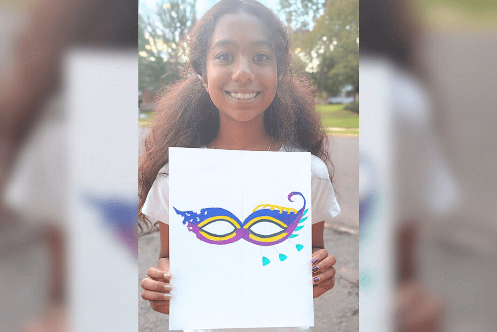 Harene holding her Venetian eye mask artwork drawn with Prismacolor pencils, focusing on symmetry and asymmetry.
