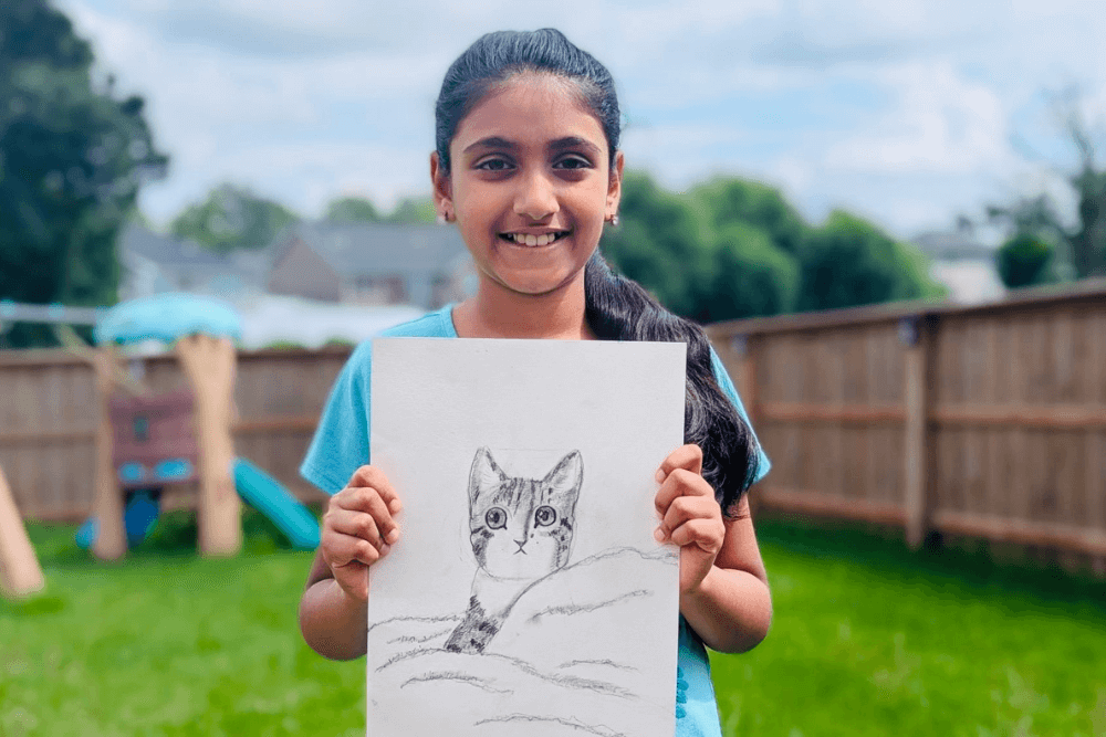 Joann holding her charcoal drawing of a cute kitten with bright eyes. From summer art camp.