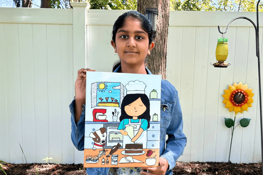 Navya holding her acrylic painting Baking Time featuring a girl chef and a puppy in the kitchen.