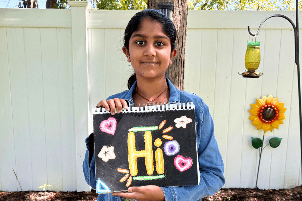 Navya holding her oil pastel artwork of a neon sign board with bold colors and glowing effects.