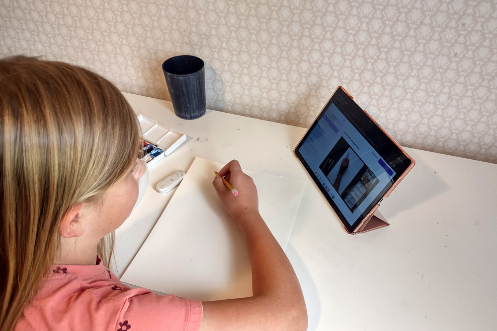 Olivia drawing during an online art class, focused on her artwork with sketching tools.