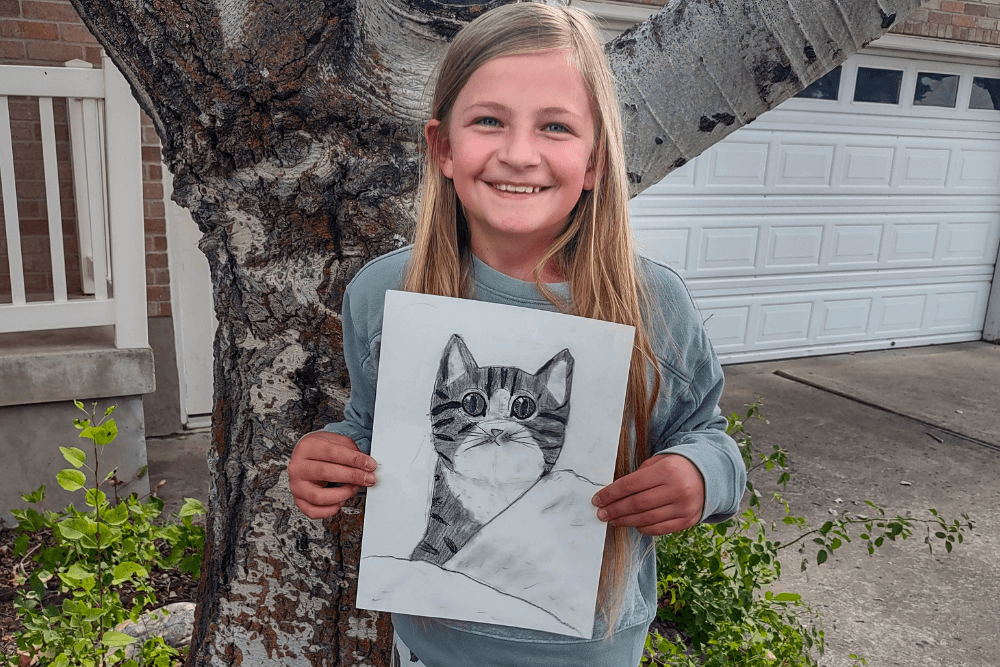 Charcoal pencil drawing of a cute kitty sitting on a bed, snuggled in sheets with big eyes, created in Nimmy's Online Art Class by Olivia.
