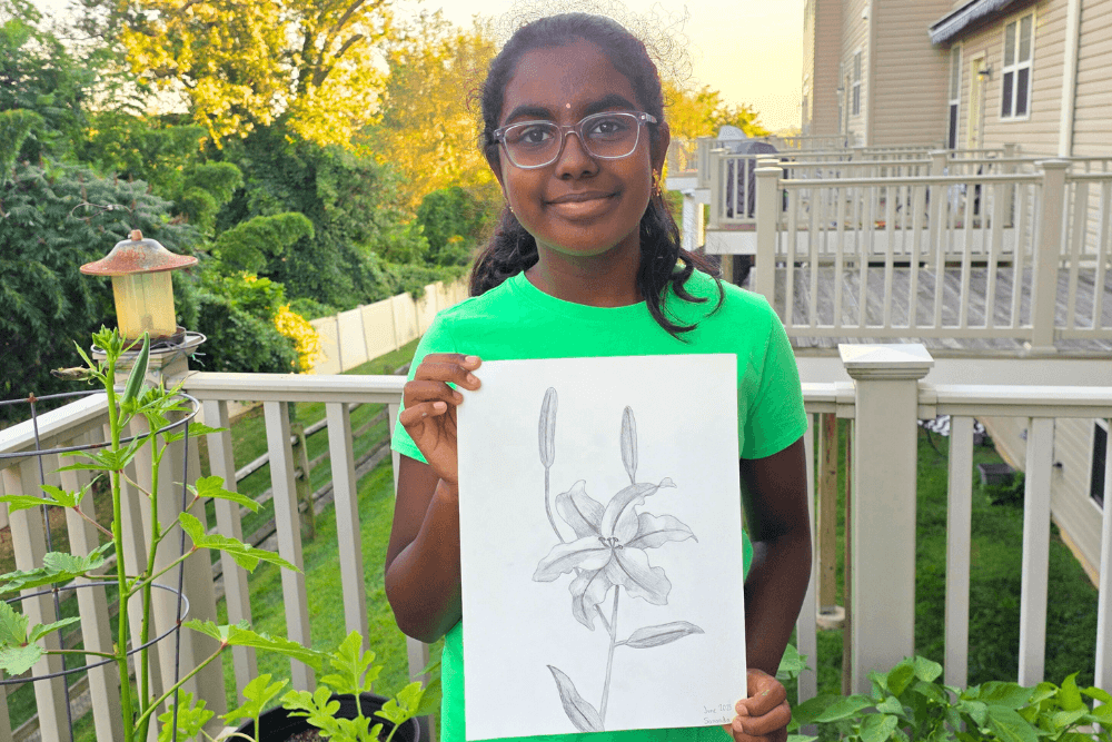 Sananda holding her pencil sketch of lilies, a detailed study of floral texture and shading.