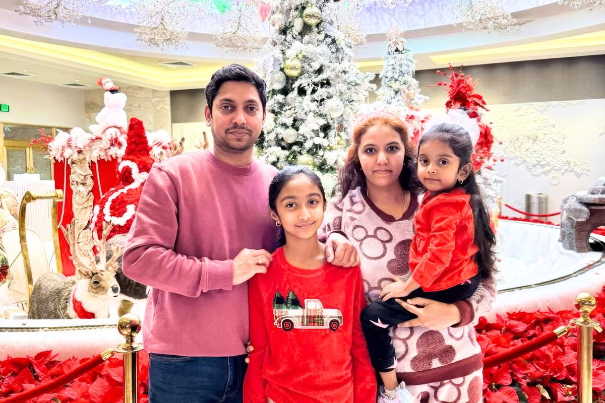 Aayushi stands with her family in front of a beautifully decorated Christmas tree, surrounded by festive red and white holiday décor, all smiling together in a joyful family moment.