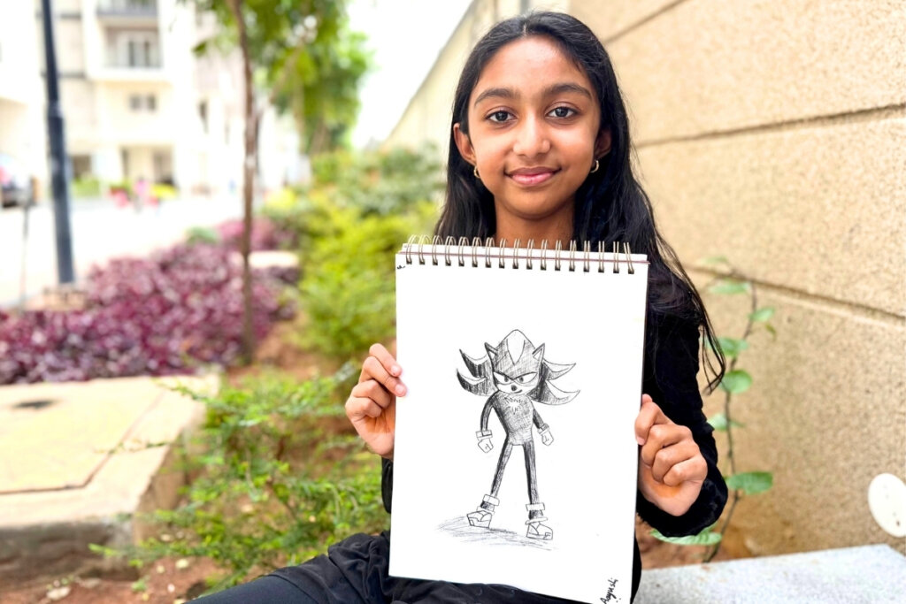 Aayushi proudly holds her charcoal drawing of Shadow from Sonic, featuring bold shading, strong contrasts, and a confident character pose in a black-and-white sketch.