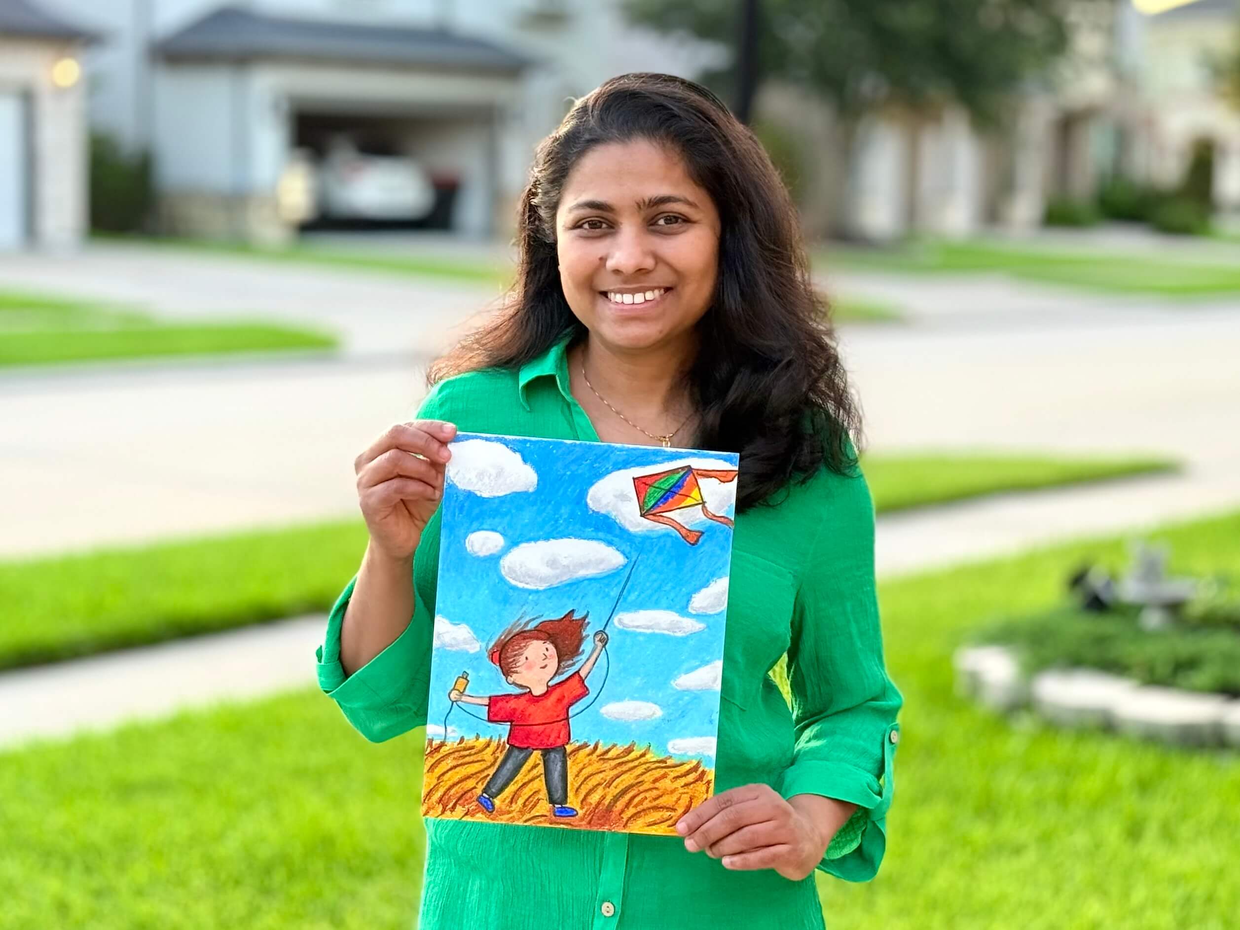 Nimmy holds a colorful oil pastel artwork of a child chasing clouds and flying a kite during a kids’ summer art camp class.