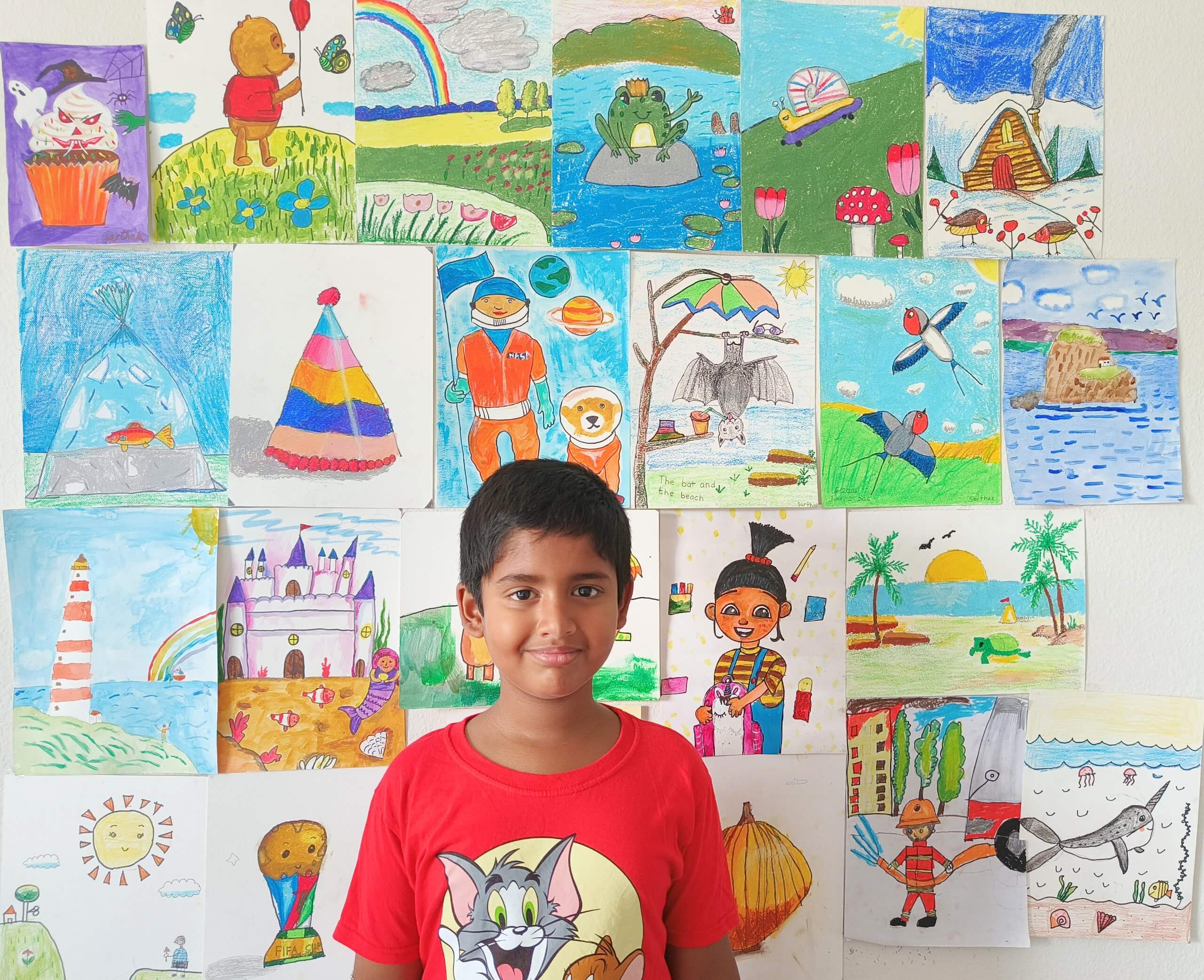 Sarthak stands smiling in front of a wall filled with his colorful artwork, featuring drawings of animals, landscapes, nature, fantasy scenes, and creative illustrations that showcase his imagination and artistic growth at Nimmy's Art.