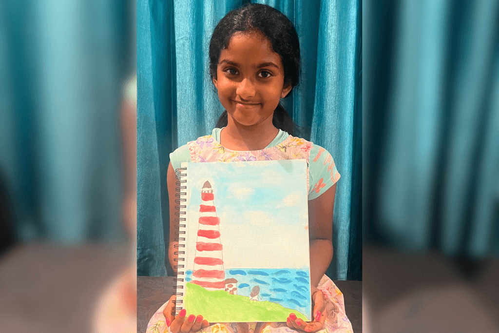 Ameya Kolachina holding her painting of a red-and-white lighthouse on a green shore beside a blue sea.
