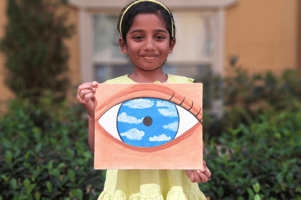 Hazel George holding her painting of a large eye with a bright blue sky and white clouds inside the iris.