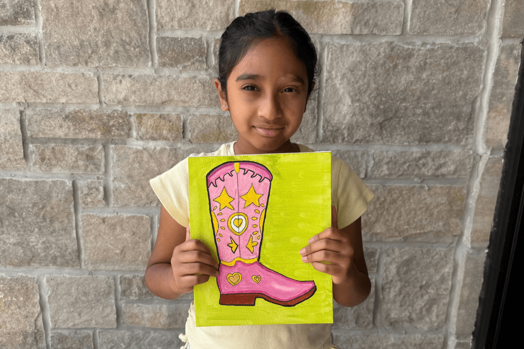 Ira Nadella holding her acrylic painting of a pink cowboy boot decorated with yellow stars and hearts on a lime-green background.