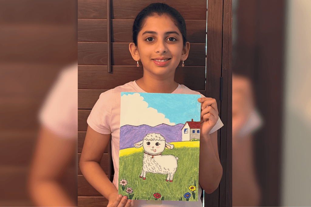 Sri Vindhya Satuluri holding her artwork of a white lamb in a flower-filled meadow with purple mountains and a small house.