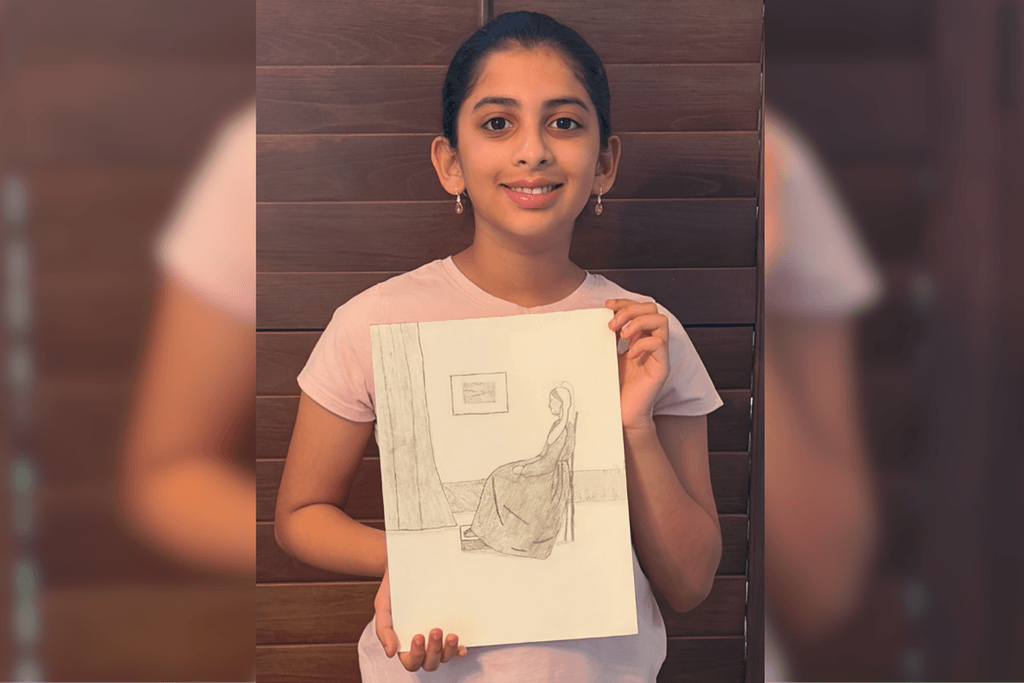 Sri Vindhya Satuluri holding her pencil drawing of a woman seated in profile beside a curtain and framed wall art.