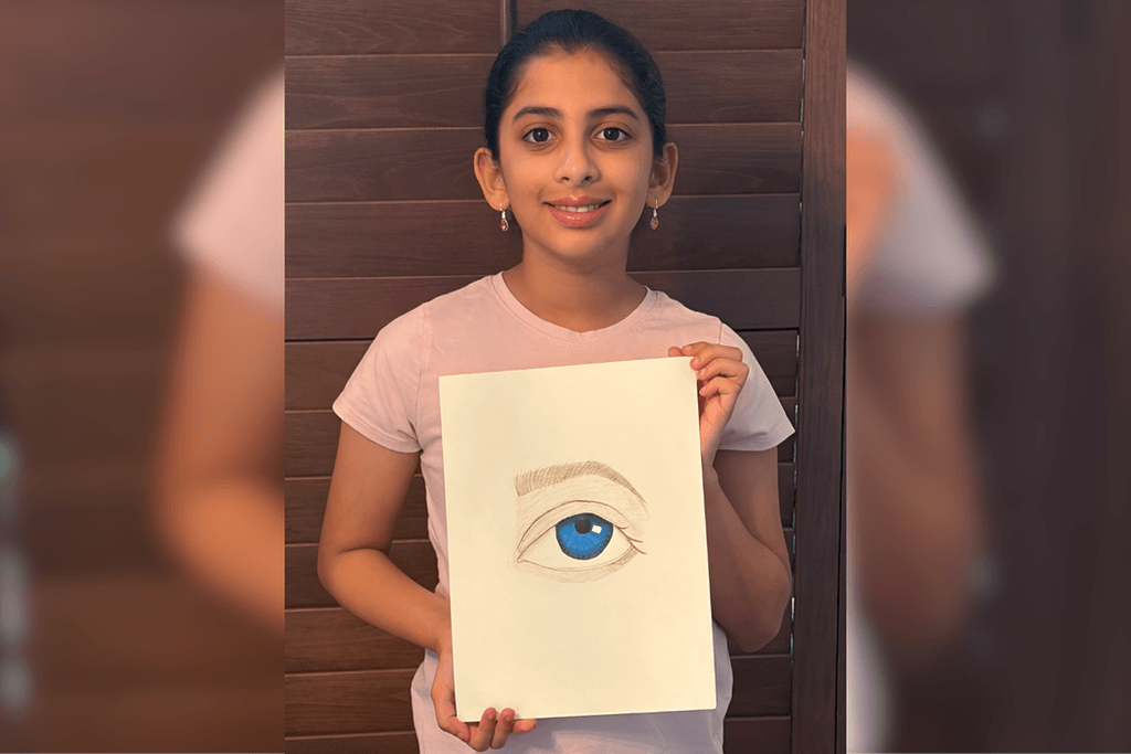 Sri Vindhya Satuluri holding her detailed eye drawing with a blue iris, white highlights, and a shaded brown eyebrow.